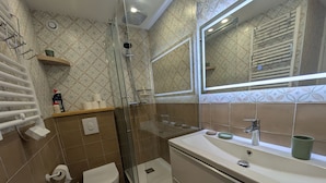 Une salle de bain moderne avec une douche à parois de verre, des toilettes, un lavabo avec un miroir et un porte-serviettes.