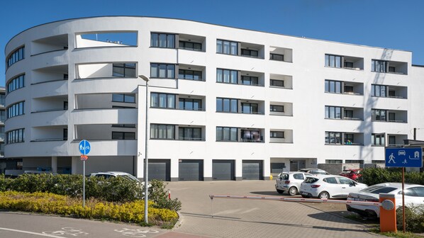 A multi-story building with a curved facade, multiple balconies, and a parking area with several cars.