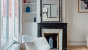 A modern living room with a white rocking chair, a fireplace, and a large window. - White Beauty, by Veeve (Paris)
