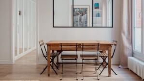 A dining area with a wooden table and chairs, a large mirror on the wall, and a radiator near the window. - White Beauty, by Veeve (Paris)