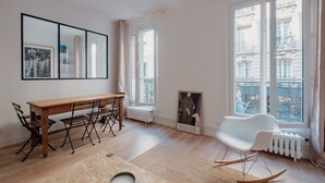 A modern living room with a wooden dining table, white rocking chair, and large windows offering a view of the city. - White Beauty, by Veeve (Paris)
