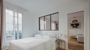 A bedroom with a large bed, a bedside table, a mirror, and a view of a balcony and another room. - White Beauty, by Veeve (Paris)