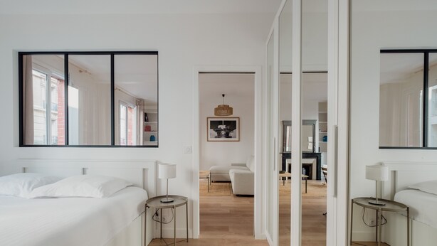 A modern hotel room with a large bed, two bedside tables, a mirror, and a view into the living area. - White Beauty, by Veeve (Paris)