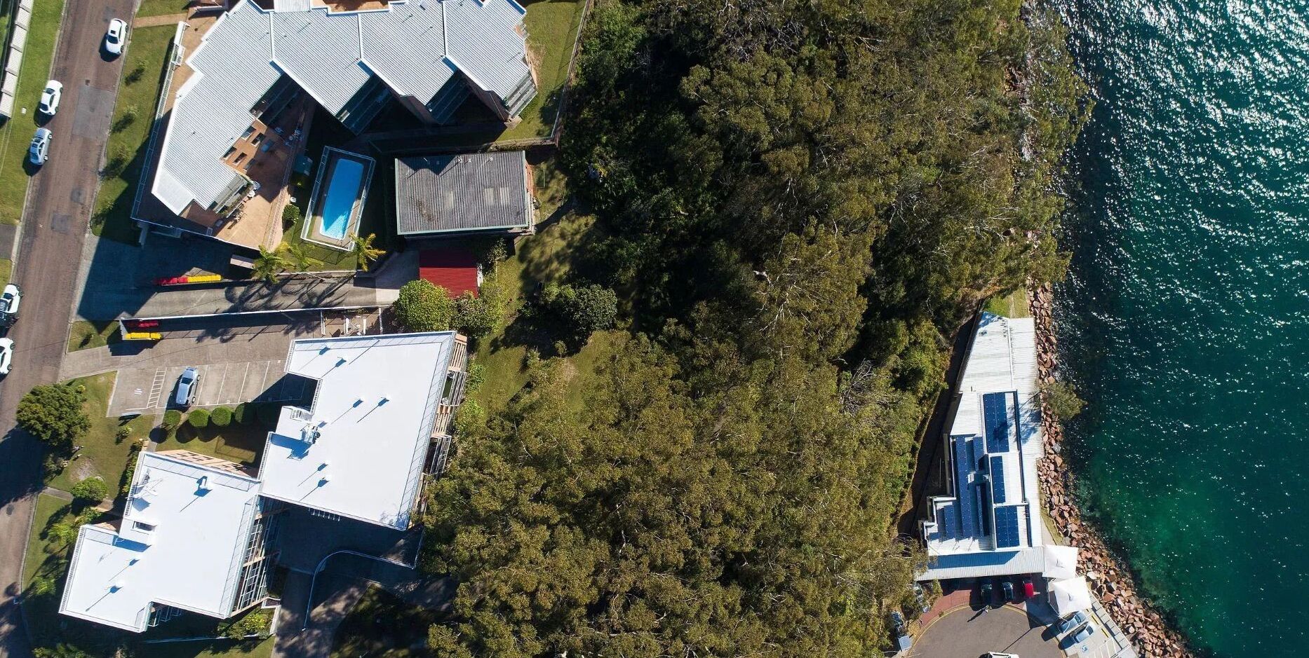 An aerial view of a coastal property with multiple buildings, a swimming pool, and a rocky shoreline.