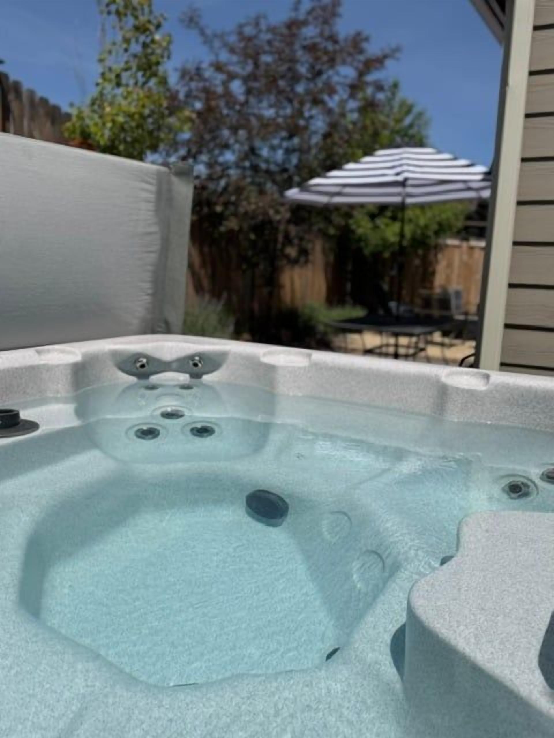 A hot tub with a clear water surface, surrounded by a wooden fence and an umbrella.