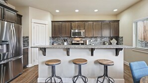 A kitchen with dark wood cabinets, stainless steel appliances, a granite countertop, and three stools.