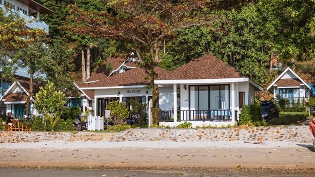 A beachfront hotel with a white facade, a covered outdoor seating area, and a sandy beach in the foreground. - Sea Escape Koh Chang (Ko Chang)