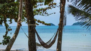 A hammock between palm trees on a beach with clear water and distant land. - Sea Escape Koh Chang (Ko Chang)