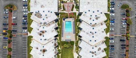 An aerial view of a hotel with a central swimming pool, multiple parking lots, and landscaped areas.