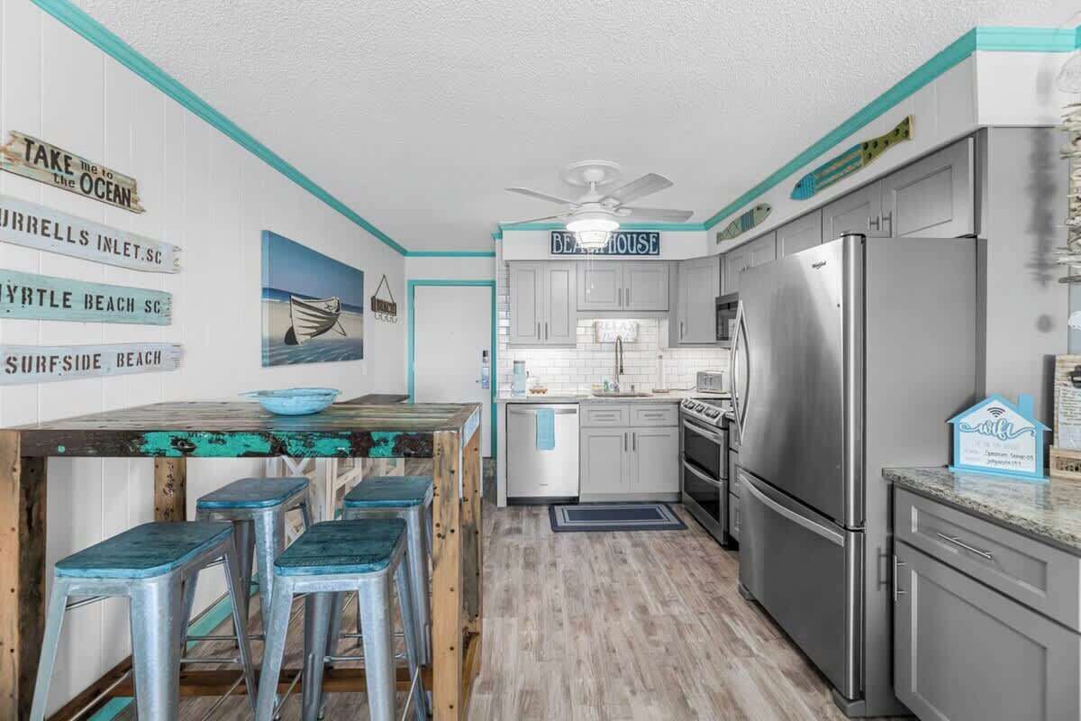 A kitchen with a wooden island, bar stools, a refrigerator, and a ceiling fan.
