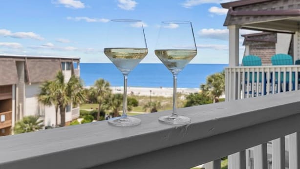 Deux verres de vin blanc sur un balcon donnant sur l’océan et la plage.