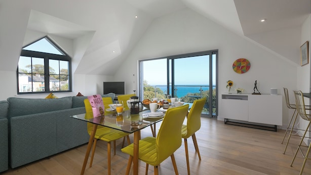 Un salón moderno con una mesa de comedor de cristal, sillas amarillas, un sofá gris y un ventanal con vistas al mar.