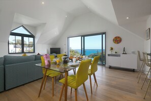 Un soggiorno moderno con tavolo da pranzo in vetro, sedie gialle, un divano grigio e un'ampia finestra vista mare.