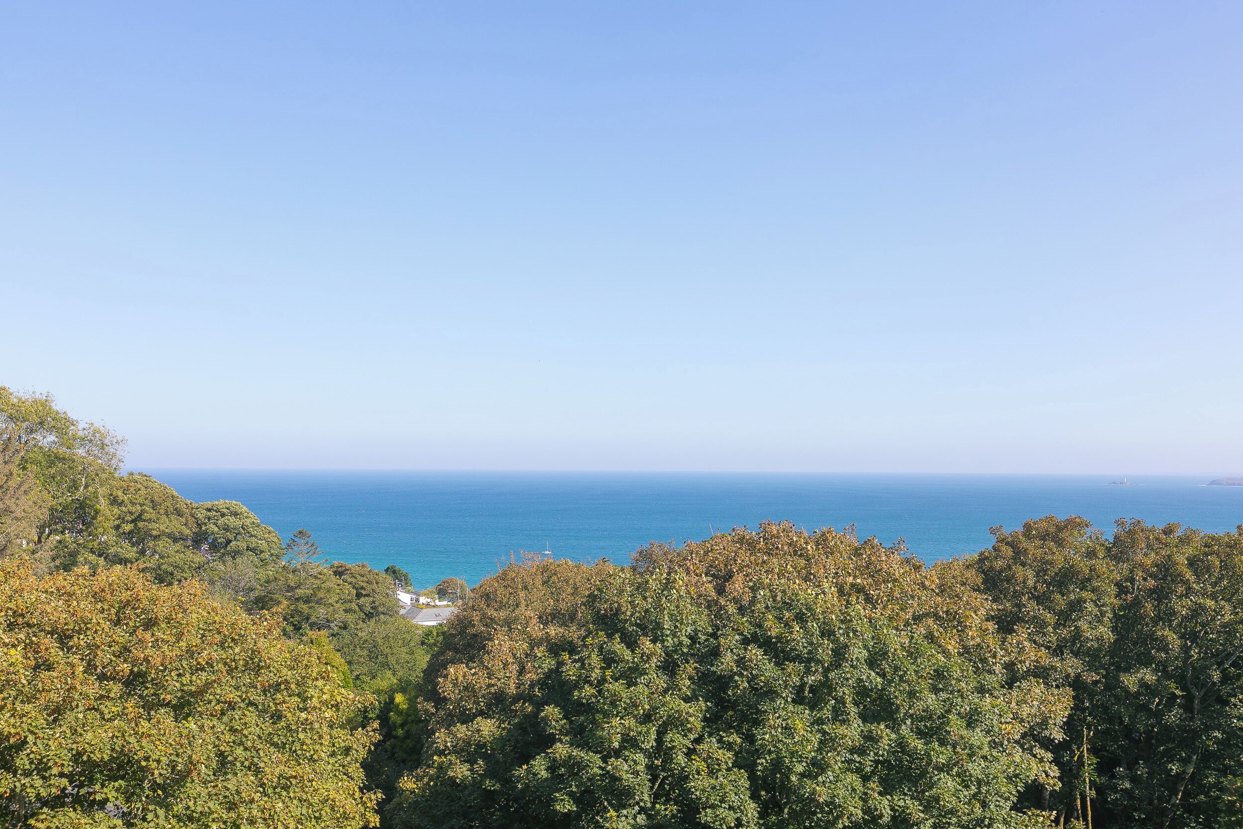 A coastal landscape with dense foliage and a clear view of the sea.