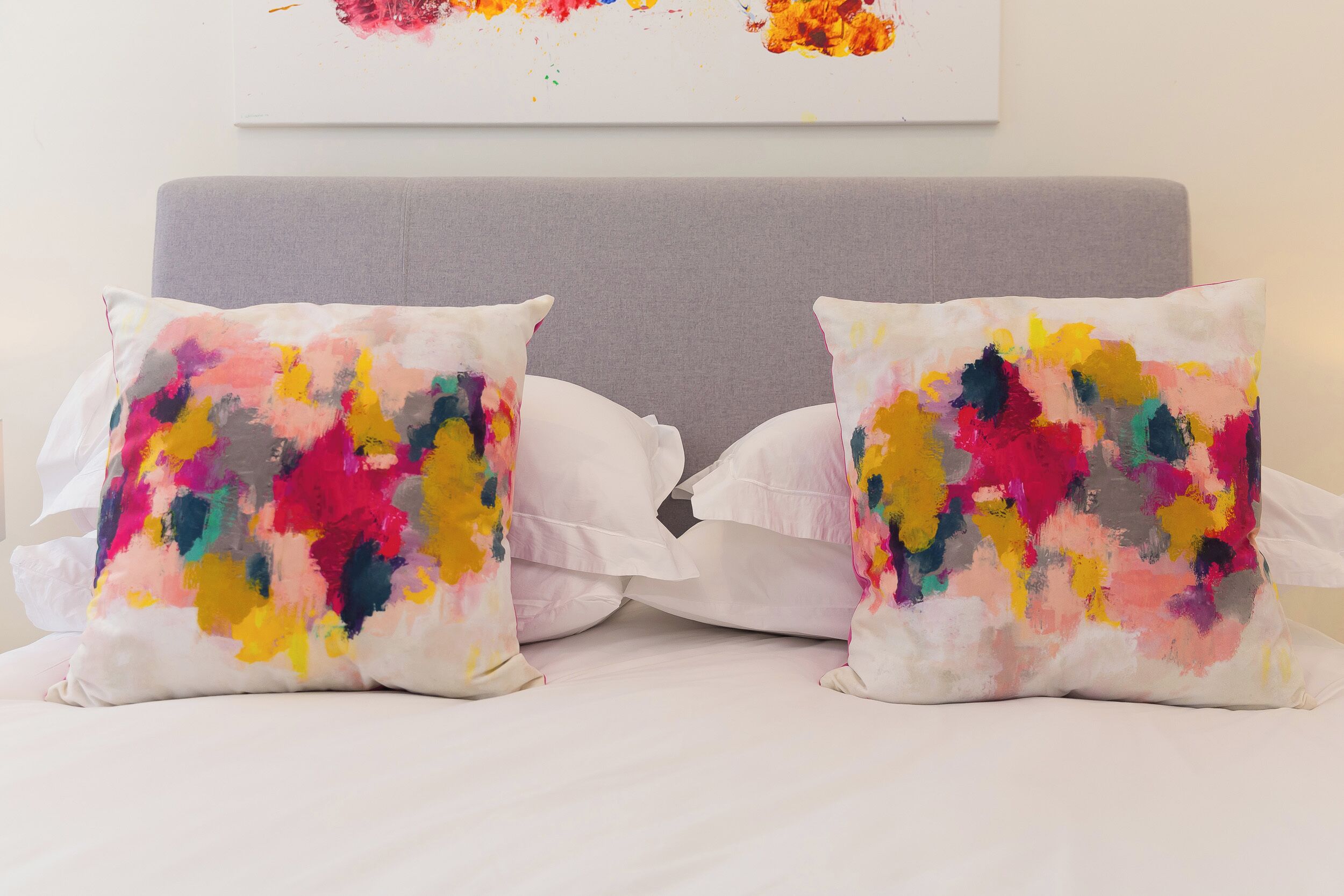 Una cama con dos almohadas coloridas y un cabecero sencillo.