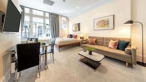 A modern hotel room with a bed, a sofa, a dining area, and a large window. - Modern Studio in Mayfair next to Hyde Park (London)