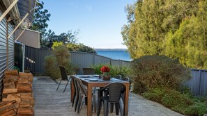 An outdoor dining area with a table set for four, surrounded by chairs, a stone wall, and a view of the sea. - Reflections - Pet Friendly Waterfront (Basin View)