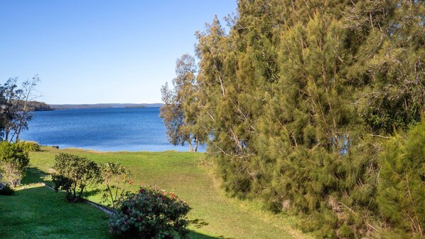 A coastal landscape with a clear view of the sea, a grassy area, and dense trees. - Reflections - Pet Friendly Waterfront (Basin View)