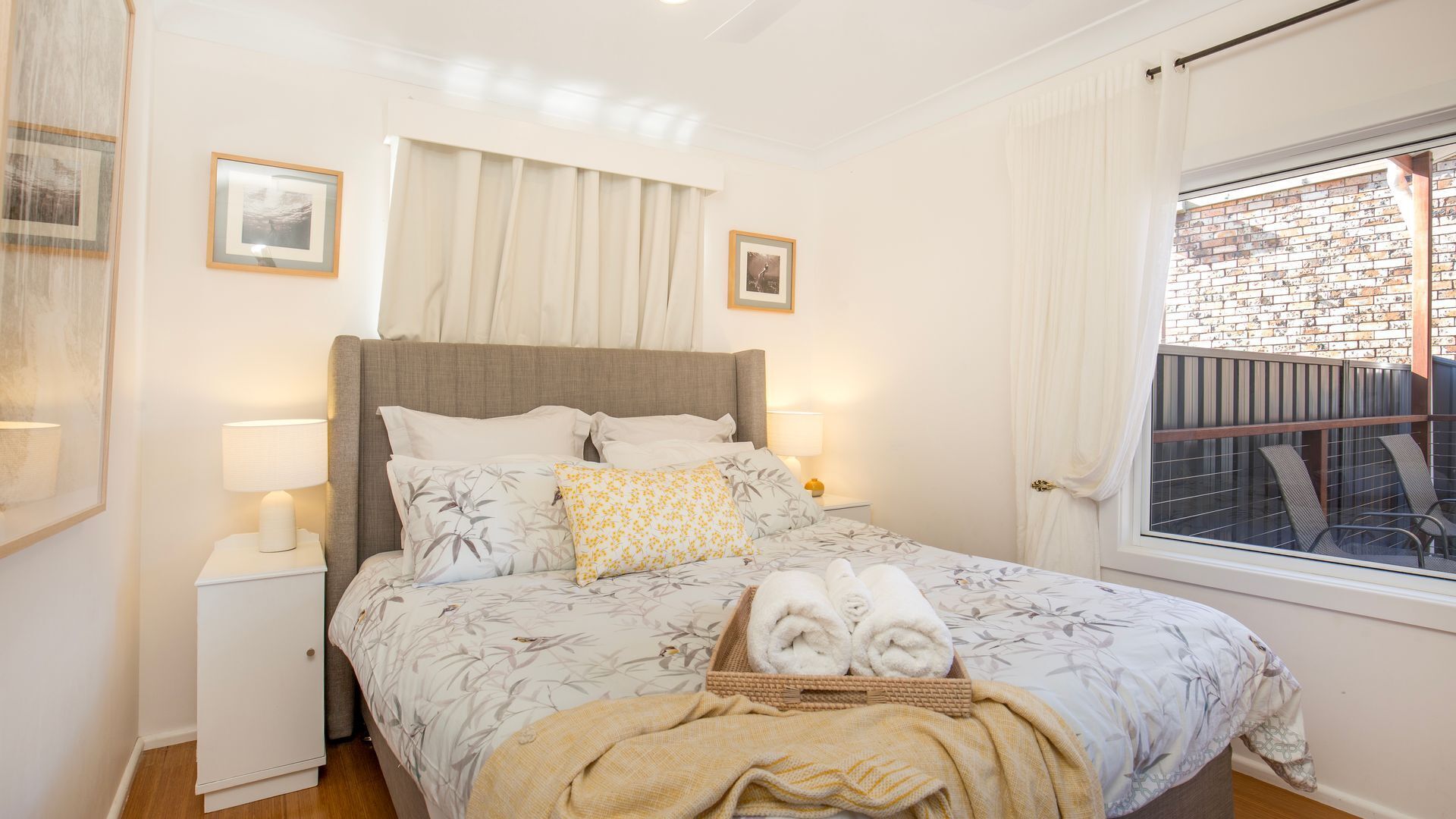 Une chambre à coucher avec un lit, des lampes de chevet, une fenêtre avec des rideaux et une vue sur un mur de briques à l’extérieur.