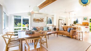 A spacious living area with a dining table, chairs, a sofa, and a kitchen in the background.