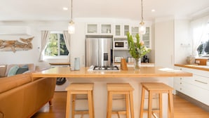 A modern kitchen with a central island, wooden stools, a refrigerator, and a coffee machine.