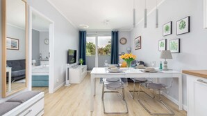A modern, open-plan living and dining area with a white table, bar stools, and a view of the outdoors.