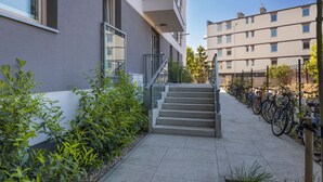A modern building with a staircase leading to a balcony, surrounded by greenery and a row of bicycles.