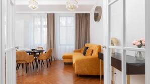 A modern living room with a sofa, dining table, chairs, and a chandelier.