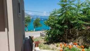 A narrow outdoor corridor with a tiled floor, a white railing, and a view of a body of water and distant mountains. - Studio on Agia Efimia Seaside (Kefalonia)