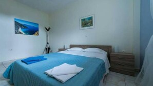A bedroom with a bed, a nightstand, a lamp, and two wall-mounted pictures. - Myrtos Cottages Polimnia (Kefalonia)