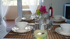 A dining table set with white plates, bowls, and glasses, a bottle of red wine, and a candle in a glass holder. - Myrtos Cottages Polimnia (Kefalonia)