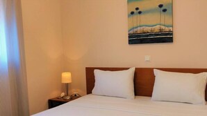 Ein Hotelzimmer mit einem Bett, weißen Leinentüchern, einem Nachttisch mit einer Lampe und einem Landschaftsbild an der Wand.