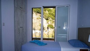A bedroom with two beds, a sliding glass door to a balcony, and a wardrobe.