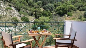 A balcony with a table set for breakfast, overlooking a mountainous landscape.