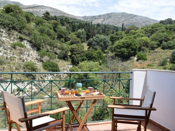 A balcony with a table set for breakfast, overlooking a mountainous landscape.