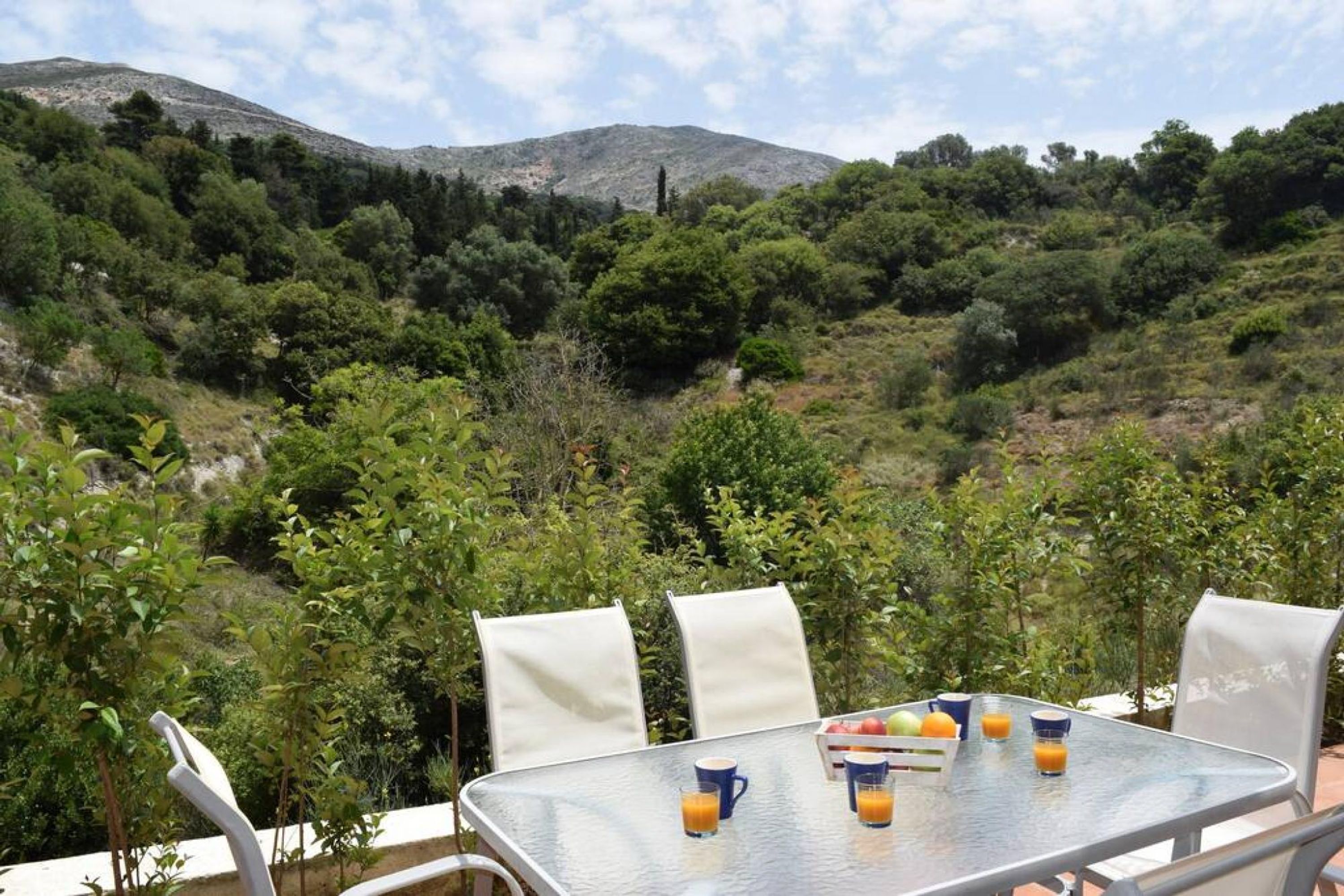 Zona d'exterior per menjar amb una taula preparada per a dues persones, envoltada de vegetació i amb les colines al fons.