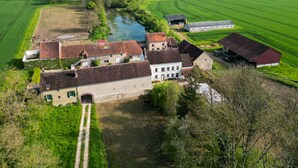 Un domaine rural comprenant plusieurs bâtiments, une rivière et de vastes champs verdoyants.