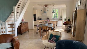 Amplia sala de estar con una escalera, una mesa de comedor con sillas, un sofá y una cocina al fondo.