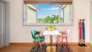 A dining area with a table and chairs, a window with a view of greenery, and a colorful rug on the floor. - Jeju West Dokchae Pension (Jeju City)