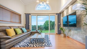 A spacious living room with a leather sofa, a zebra-patterned rug, and a large window offering a view of greenery. - Jeju West Dokchae Pension (Jeju City)