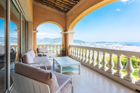 A balcony with a white table and chairs, a view of the city and mountains.