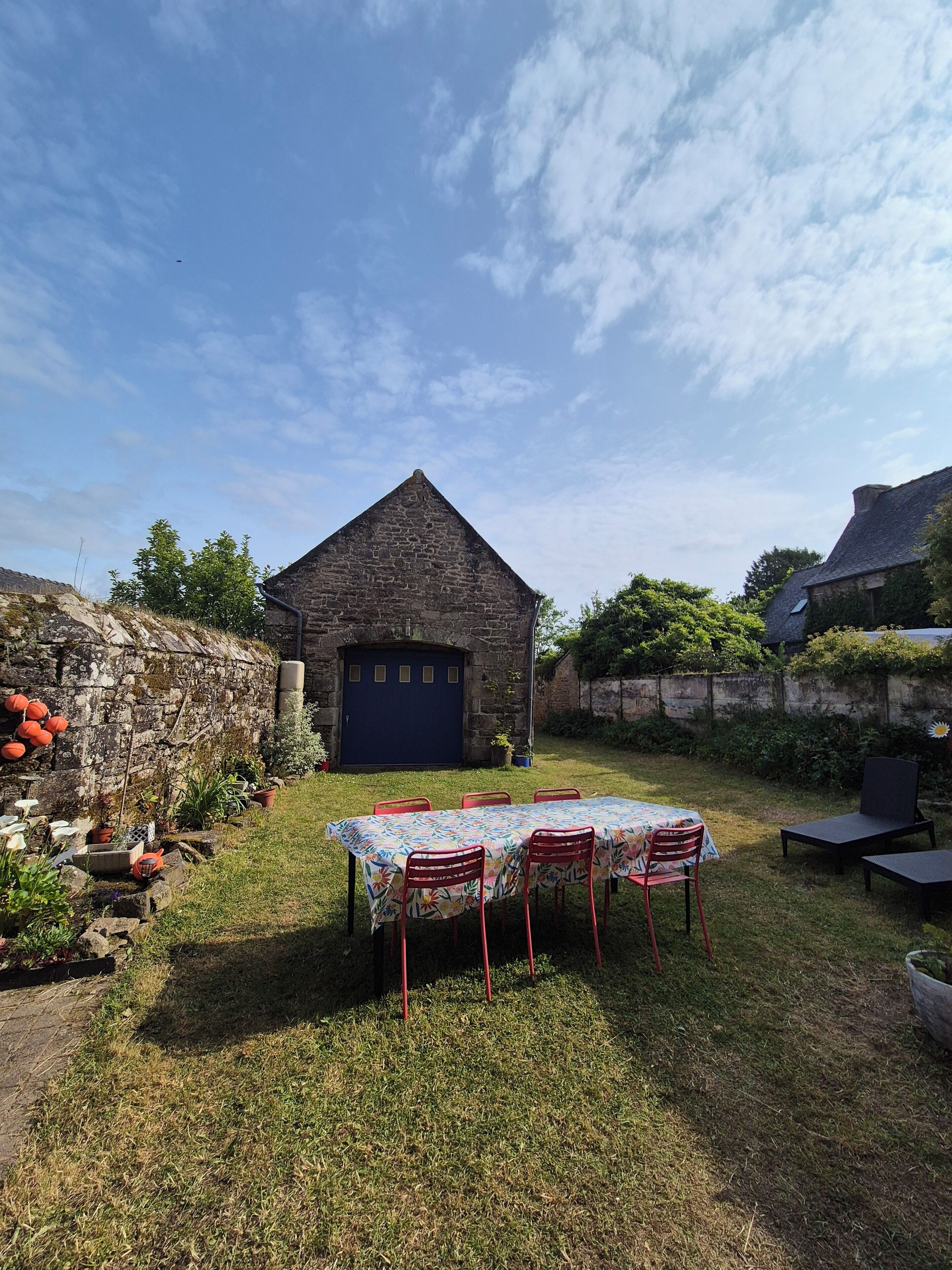 A stone building with a blue door, a table with chairs, and a garden area with plants and a pathway.