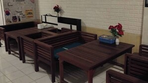 A dining area with wooden furniture, a white brick wall with artwork, and a small table with a vase of flowers.