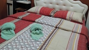 A neatly made bed with a white headboard, red and beige bedding, and two green towels.