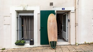 A wooden surfboard leaning against a building with a green door and a window with metal bars. - Surfing-house Biarritz (Biarritz)