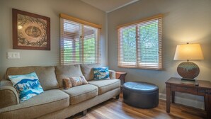 Uma sala de estar com sofá, apoio para os pés e uma luminária em uma mesinha lateral.