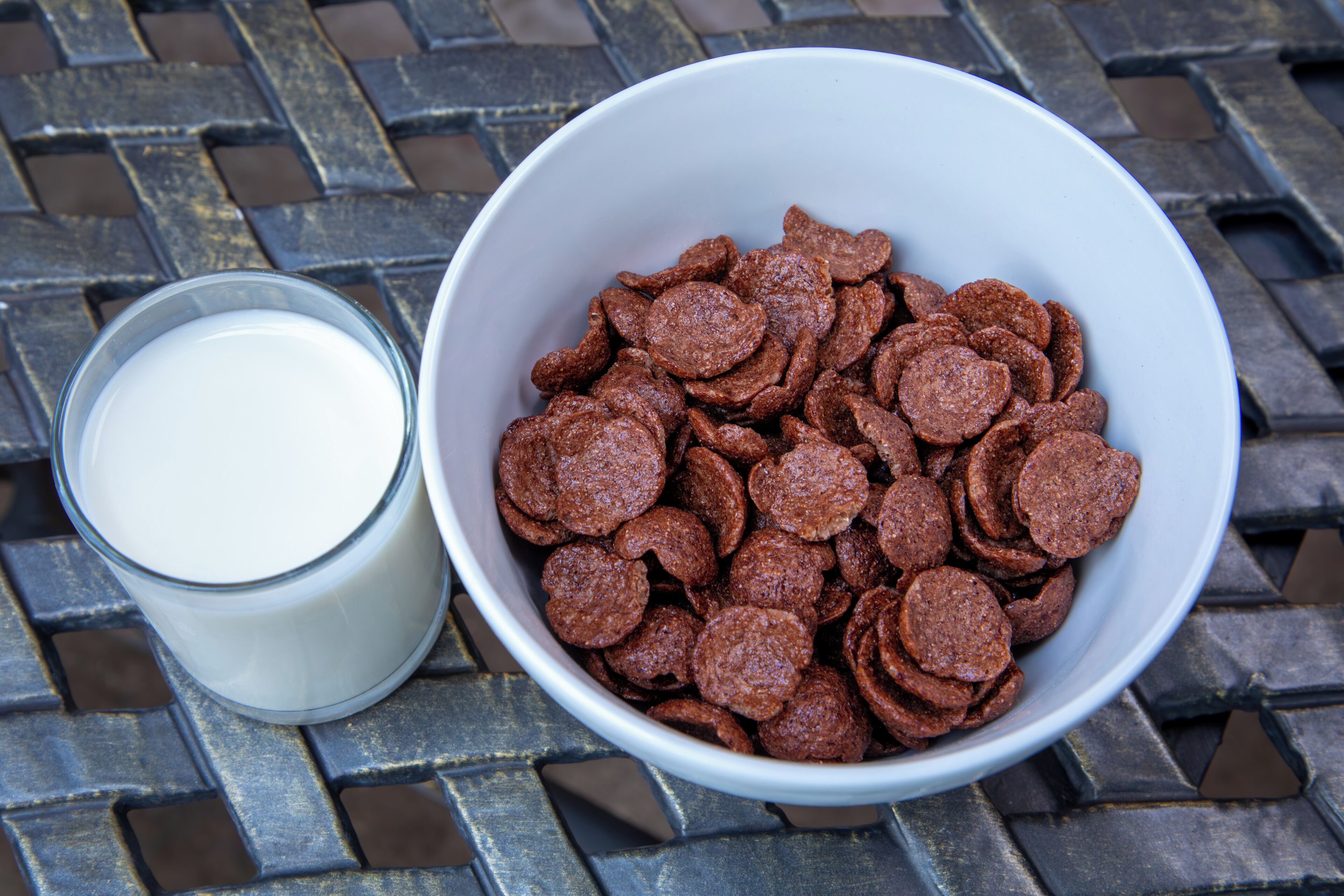 Eine Schüssel mit Müsli neben einem Glas Milch auf einer Metalloberfläche.