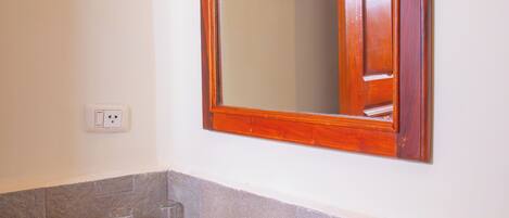 Un baño con un lavabo blanco, un espejo con marco de madera y una cesta de artículos de aseo.