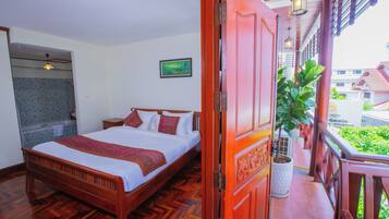 Ein hölzernes Bett mit weißer und roter Bettdecke, ein Nachttisch, ein Blumentopf und ein Balkon mit Geländer.