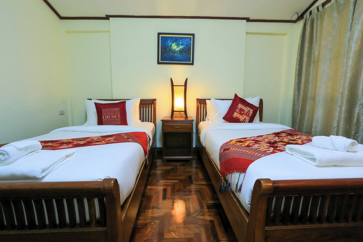 A hotel room with two beds, wooden headboards, a nightstand with a lamp, and a painting on the wall.